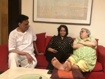 Indoor scene: Ajay Rungta (Dadu), his wife (Ma), and Aarti are seated comfortably on a red sofa, appearing to be in conversation.