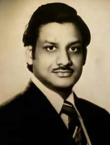 A sepia-toned formal portrait of a young Ajay Rungta (Dadu) in a suit and tie, looking directly at the camera with a gentle smile.