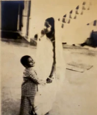 Vintage black and white photo of a young Ajay Rungta (Dadu) smiling and holding hands with his mother.