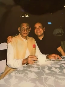 A warm photograph of Ajay Rungta (Dadu) in a traditional Indian vest and CKD in a dark shirt, smiling together at a dinner table.