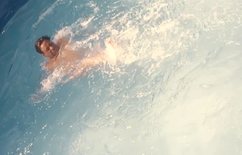 Overhead view of Ajay Rungta (Dadu) swimming with energy in a bright blue pool, playfully nicknamed 'Phelps' for his splashing.
