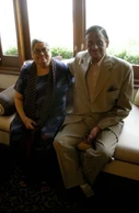Ajay 'Dadu' Rungta and his wife Ma (Chinu) seated on a sofa, smiling. Dadu is in a suit, Ma in a patterned blue dress and scarf.